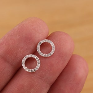 Puede incluir: Un par de pendientes de plata con un diseño circular. Los círculos están engastados con pequeñas piedras transparentes.