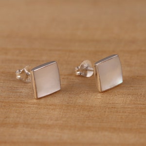 May include: A pair of silver square earrings with a white mother of pearl inlay.