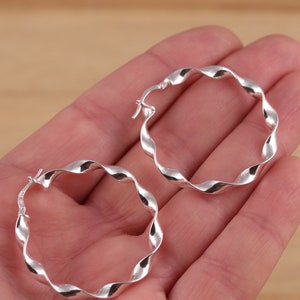 May include: A pair of silver hoop earrings with a twisted design. The earrings are made of metal and have a shiny finish.