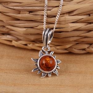 Puede incluir: Un collar de plata con un colgante de sol con una piedra de ámbar.