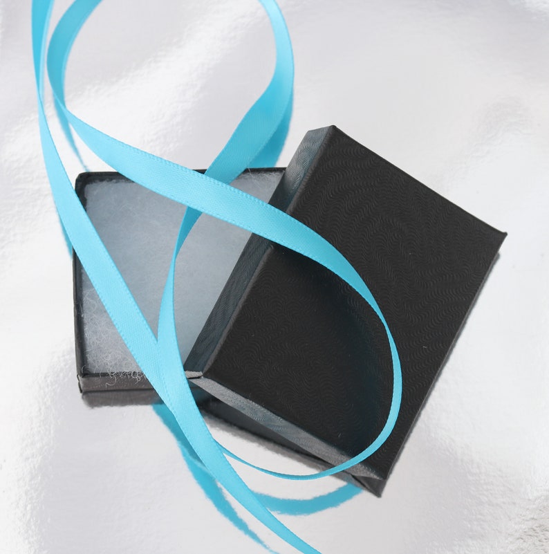 May include: A black gift box with a blue ribbon tied around it. The box is open and the inside is lined with white felt.