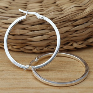 May include: A pair of silver hoop earrings. The earrings are round and have a slightly thicker band. The earrings are closed with a hinged clasp.