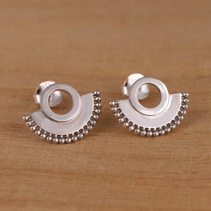 May include: A pair of silver earrings with a circular design and a beaded edge. The earrings are in the shape of a half-circle with a smaller circle cut out in the centre.