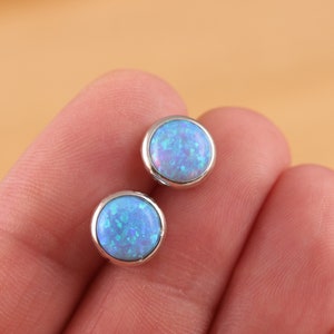 Könnte beinhalten: Ein Paar silberne Ohrstecker mit runden blauen Opal-Steinen.