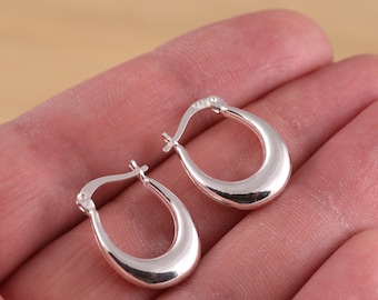 May include: A pair of polished silver hoop earrings. The earrings have a smooth, rounded design and a secure clasp closure. The hoops are a classic jewellery style.