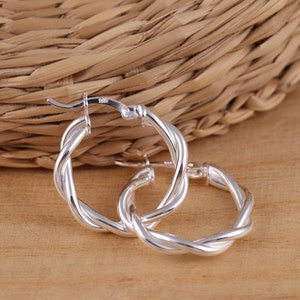 Può includere: Orecchini a cerchio in argento con un design intrecciato. Gli orecchini sono semplici ed eleganti.