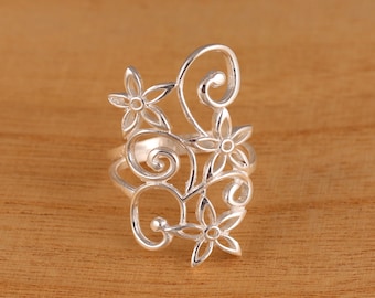 May include: A silver ring with a delicate floral design. The ring features intricate swirls and flowers, creating a delicate and feminine look.