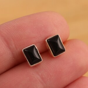 Könnte beinhalten: Ein Paar silberne Ohrstecker mit schwarzen quadratischen Edelsteinen.