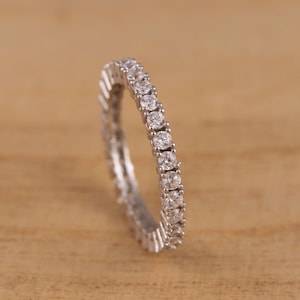 May include: A silver band ring with a row of small, clear, round gemstones.
