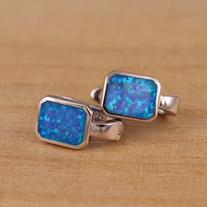Könnte beinhalten: Ein Paar silberne Ohrringe mit blauen Opal-Steinen. Die Ohrringe sind rechteckig und haben ein schlichtes Design.