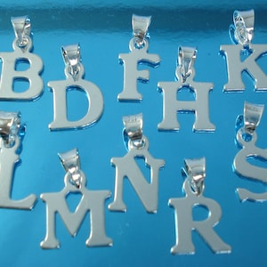 May include: A selection of silver alphabet letter pendants, including B, D, F, H, K, L, M, N, R, and S. Each pendant has a small loop at the top for attaching to a chain or bracelet. The pendants are displayed on a reflective blue surface.