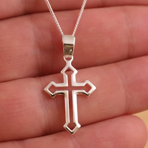 Può includere: Una collana con catena d'argento con un delicato ciondolo a forma di croce traforata. La croce ha un design semplice ed elegante.