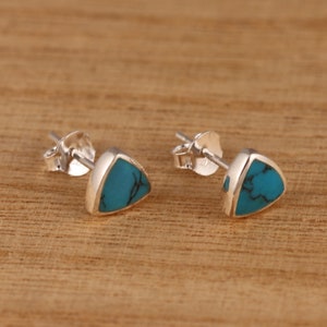 Op de afbeelding: Een paar zilveren driehoekige oorbelletjes met turquoise stenen.