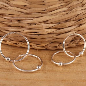 May include: Three silver hoop earrings with small ball accents. The earrings are arranged on a woven surface.