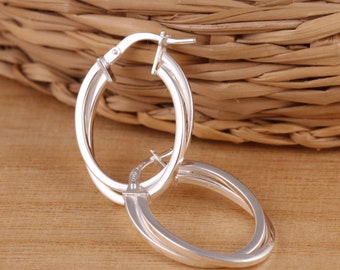 May include: Silver hoop earrings with a double-loop design. The earrings are made of polished silver and have a smooth finish.