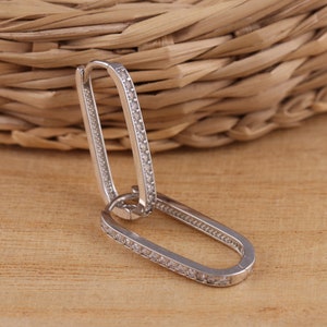 Peut inclure: Boucles d'oreilles créoles en argent de forme rectangulaire avec une rangée de pierres de zircone cubique transparentes autour du bord.