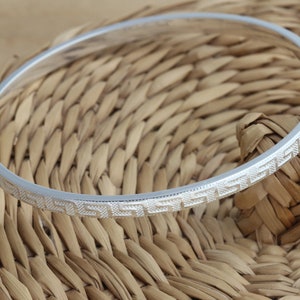 May include: A silver bangle bracelet with a geometric pattern around the edge.