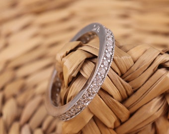 Puede incluir: Un anillo de banda de plata con una fila de pequeñas piedras transparentes engastadas en la banda.
