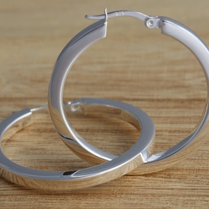 May include: A pair of silver hoop earrings with a thick, flat design. The earrings are made of metal and have a polished finish.
