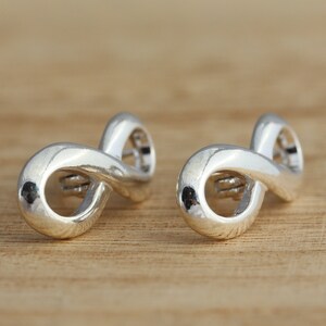 May include: A pair of silver infinity symbol earrings. The earrings are made of a smooth, shiny metal and have a simple, elegant design.