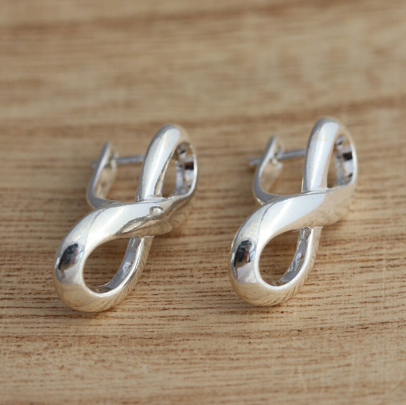 May include: A pair of silver infinity symbol earrings. The earrings are made of a smooth, shiny metal and have a simple, elegant design.