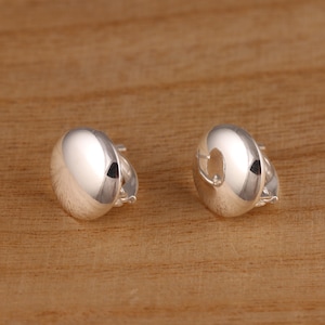 May include: A pair of silver hoop earrings with a smooth, rounded design. The earrings are made of metal and have a polished finish.