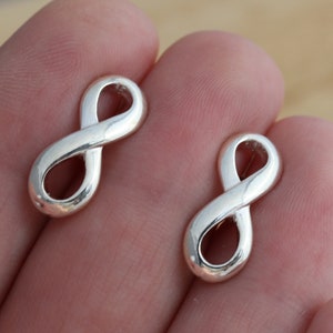 May include: Two silver infinity symbol earrings. The earrings are small and delicate, and they are perfect for everyday wear.