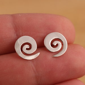 Puede incluir: Un par de pendientes de plata con diseño de espiral. Los pendientes son pequeños y delicados, con un diseño sencillo.