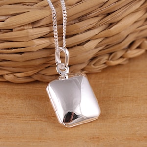 May include: A polished silver locket pendant with a square shape, hanging from a delicate chain. The locket reflects the surrounding environment, and the chain is approximately 18 inches long. The pendant is a classic piece of jewelry.