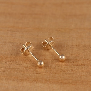 May include: A pair of gold ball stud earrings. The earrings have a simple design with a small, round ball at the end of a post.