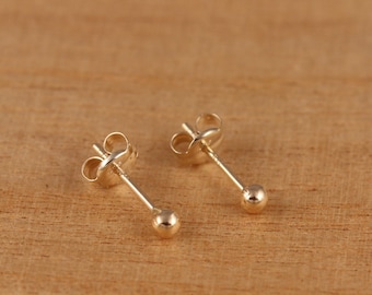 May include: A pair of gold ball stud earrings. The earrings have a simple design with a small, round ball at the end of a post.