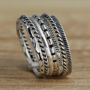 May include: A silver ring featuring five bands, each with a distinct textured design. The bands are layered on top of one another, resulting in a unique and stylish appearance.