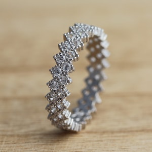 Può includere: Un anello a fascia d'argento con un motivo a chevron di piccole pietre di zircone cubico trasparenti.