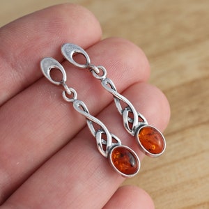 May include: A pair of silver dangle earrings with amber gemstones. The earrings feature a Celtic knot design.