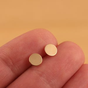 May include: A pair of small, round, gold-colored earrings. The earrings are simple and minimalist in design.