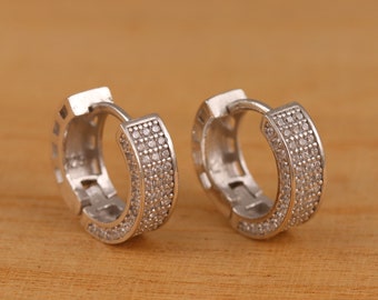 May include: A pair of silver hoop earrings with a row of small clear cubic zirconia stones around the edge.