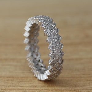 Puede incluir: Un anillo de banda de plata con un patrón de chevron de pequeñas piedras de circonita cúbica transparentes.