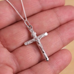 May include: A silver chain necklace with a silver crucifix pendant. The crucifix features a detailed depiction of Jesus Christ.