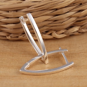 May include: Silver hoop earrings with a unique, angular design. The earrings are made of a smooth, polished metal and have a simple, modern style.