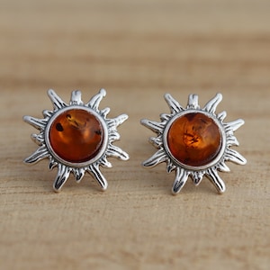 May include: A pair of silver sunburst earrings with amber stones in the centre.