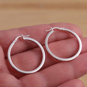 May include: A pair of silver hoop earrings. The earrings are simple and elegant, with a smooth, polished finish.