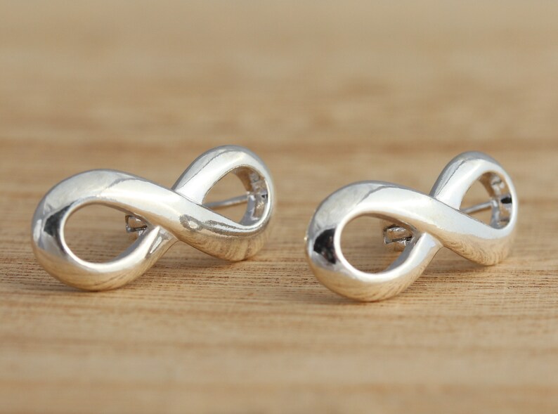 May include: A pair of silver infinity symbol earrings. The earrings are made of a smooth, shiny metal and are shaped like the infinity symbol.
