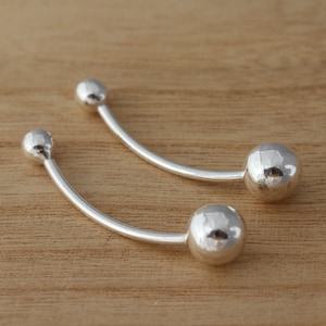 May include: A pair of silver curved bar earrings with round ball ends.