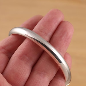 Op de afbeelding: Een eenvoudige zilveren armband, getoond op een hand, met een gladde, gepolijste afwerking.