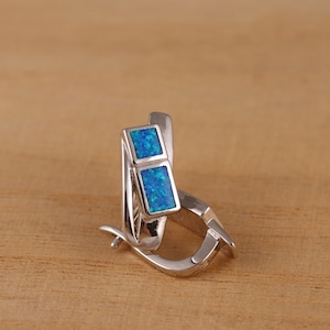 May include: Silver hoop earrings with two square blue opal stones.