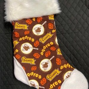 May include: A Christmas stocking featuring the San Diego Padres logo and team colors. The stocking has a brown background with the Padres logo and text in orange and white. The top and toe of the stocking are white.