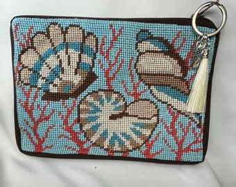 A completed Sea shell needlepoint purse/cosmetic bag. It has a silky handmade cream color tassel,an antique heart charm and a “word” charm