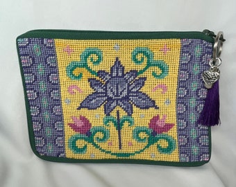 A finished needlepoint purse/cosmetic bag with lotus flower in the center. It has a deep purple tassel, a  heart charm and &quot;word&quot; charm..