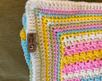 Crochet baby blanket. Think “Bunny Tracks”. It reminds me of Easter eggs. Its approximately 27 inches x 24.5 inches. White,pink,teal,yellow.