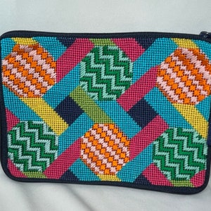 May include: A colorful needlepoint clutch bag with a geometric pattern of circles and stripes in shades of blue, green, pink, orange, and yellow. The bag has a zipper closure and a tassel.